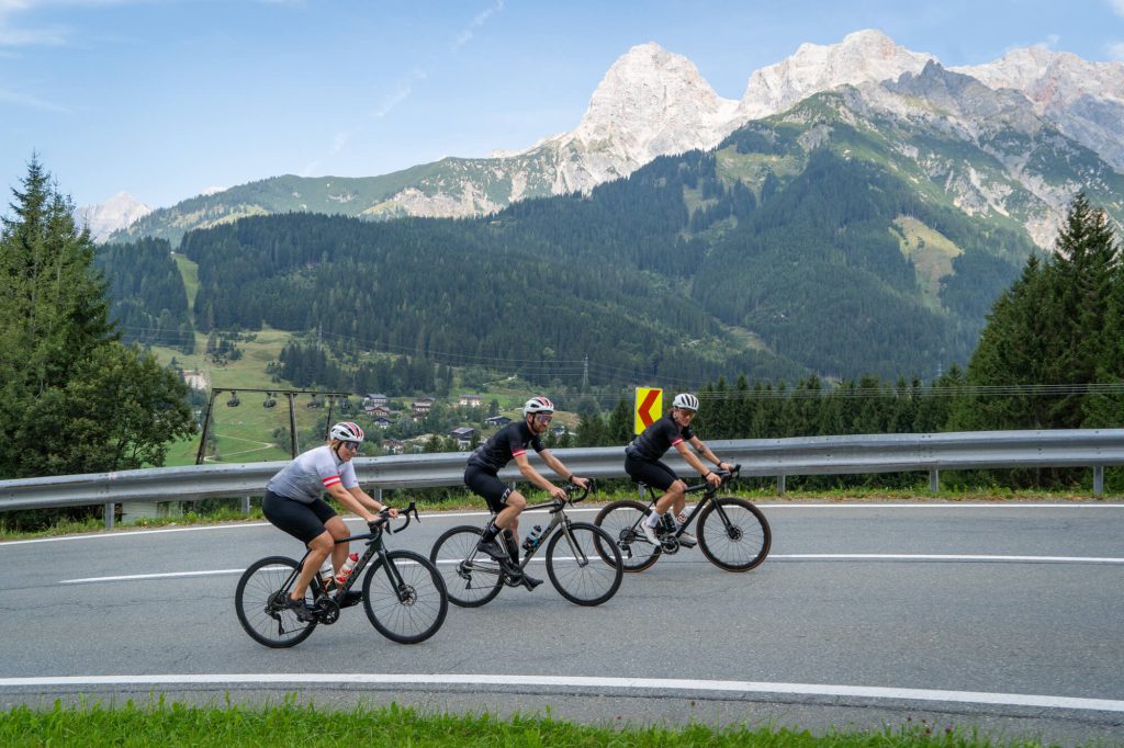 Drei Rennradfahrer auf Alpenstraße bei Saalfelden inmitten einer Radsport-Gruppe auf Langstrecke